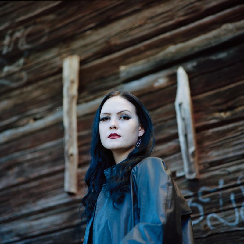Evaeuforia dressed as death, looking ominously down at the camera, standing in front of a large barn made of old wood.