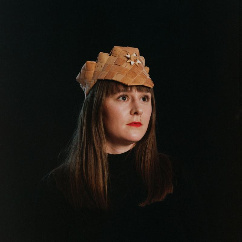 Anna wearing a traditional handcrafted birch bark hat, surrounded by black.