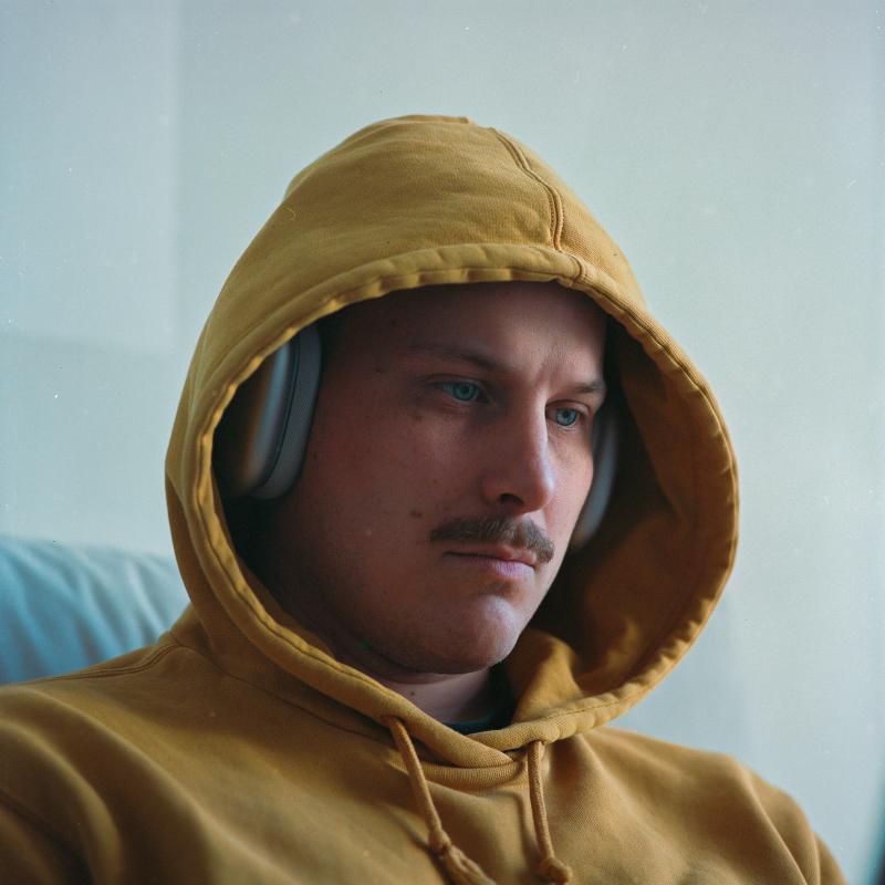Samis face inside a yellow hoodie, his piercing blue eyes staring down and to the right.