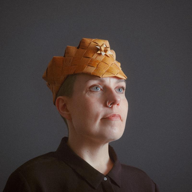 Niina wearing a traditional handcrafted birch bark hat. Dignified pose, calm evening light.