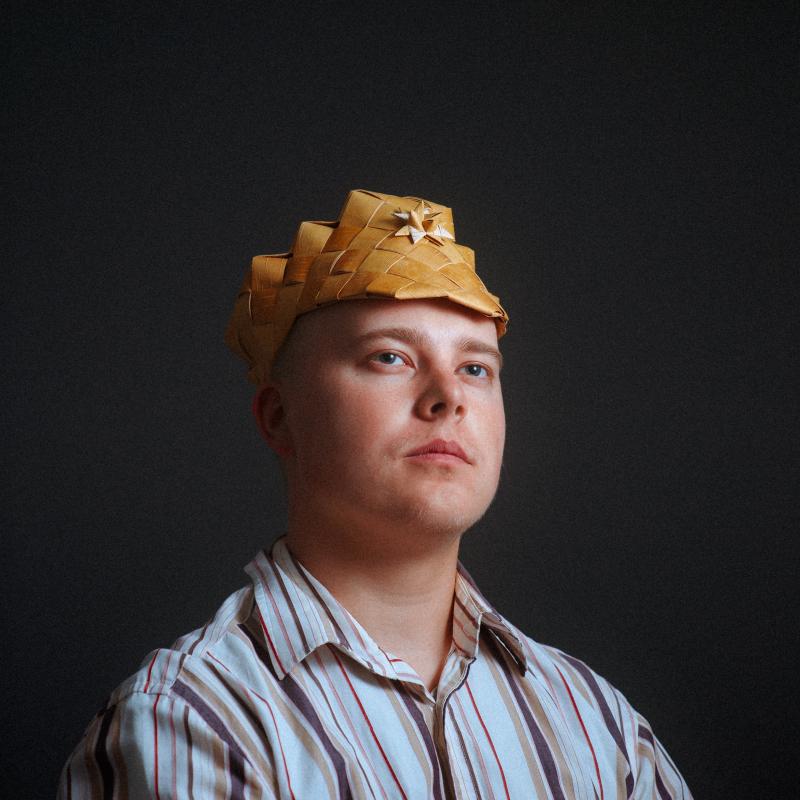 Antti wearing a traditional handcrafted birch bark hat. Evening light, dignified pose.